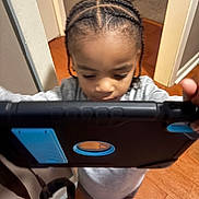 Easton is registered to the contest to win money with this photo: child, tablet, braided_hair, indoors, flooring, wall, technology, person, game, focus, young, standing, gray_clothing, feet, candid, device, hand, brown_floor, home, curiosity