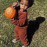 child, toddler, pumpkin, grass, outdoor, brown_clothing, holding, shadow, field, autumn, cute, person, young_child, nature, daylight, standing, pumpkin_patch, screen_screenshot, mobile_phone, apps