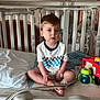 bandage, bed, checkered_pattern, child, crib, expression, face, fire_truck, furniture, healthcare, hospital, indoor, light, medical_equipment, medical_tube, person, sippy_cup, toddler, toy, white_shirt