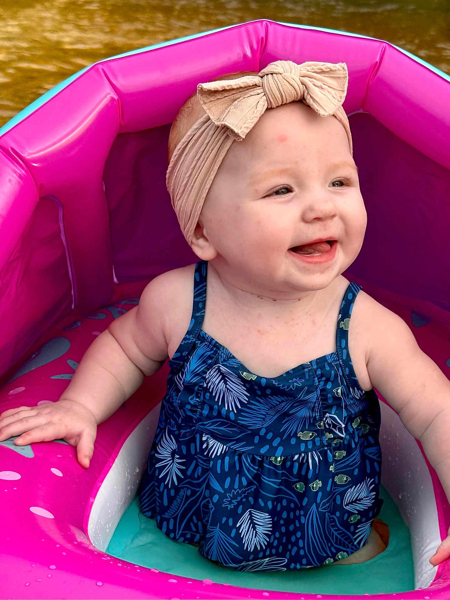 Lexi is registered to the contest to win money with this photo: baby, child, smiling, headband, swimsuit, inflatable_pool, water, pink, blue, happy, summer, outdoor, cute, sitting, playful, toddler, infant, skin, arms, fun