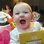 Lexi is registered to the contest to win money with this photo: baby, background, bag, child, clothing, expression, face, family, food, hand, happy, home, indoor, package, pajamas, person, person_holding, phone, smile, table