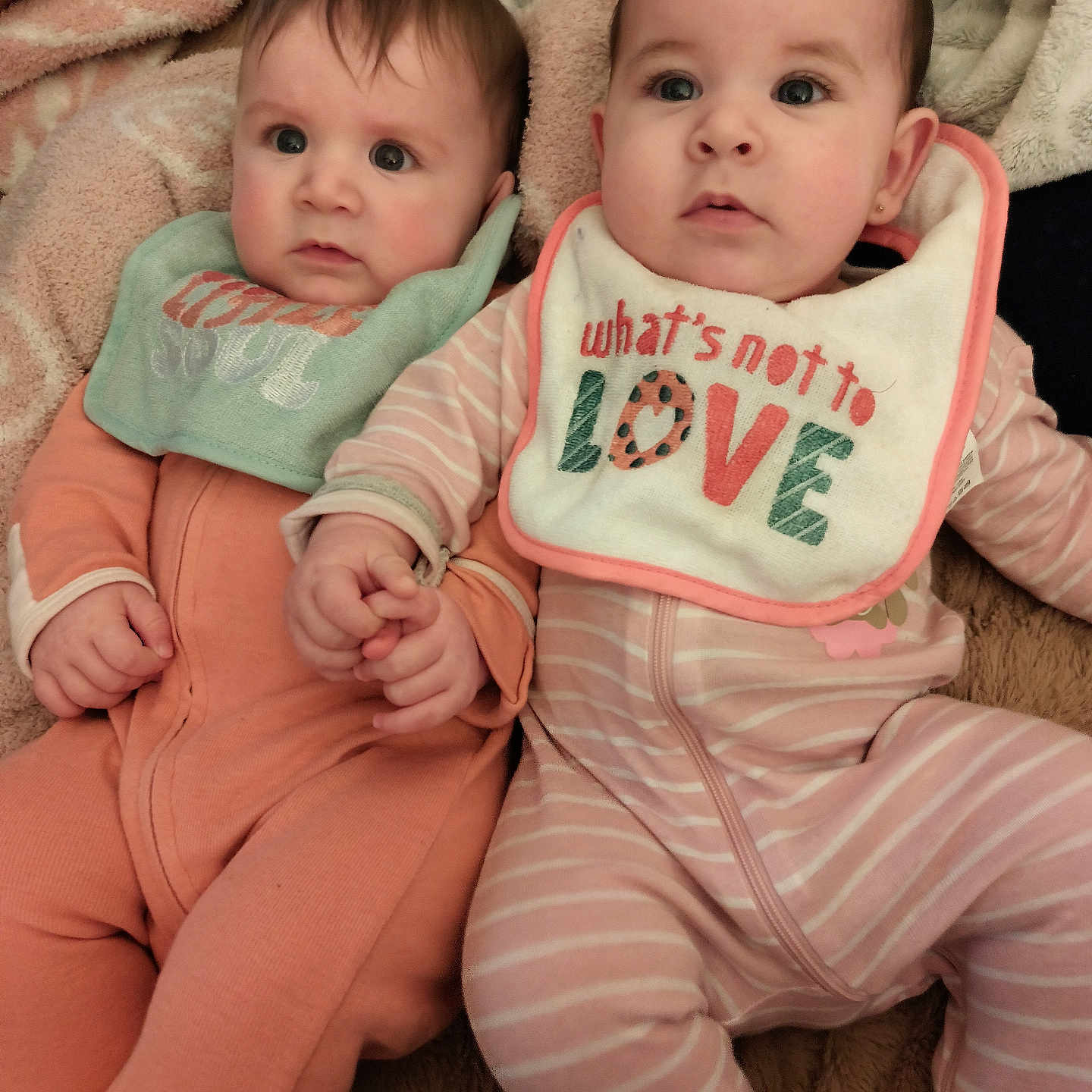 Leah Natalia joined the competition — help win amazing prizes! baby, bib, blanket, child, cute, expression, eyes, face, holding_hands, indoor, infant, lying_down, newborn, pajamas, peach, pink, sleepwear, soft_texture, toddler, two_children