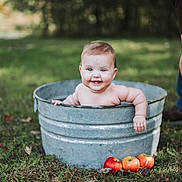 Iris joined the competition — help win amazing prizes! baby, child, metal_tub, outdoor, grass, apples, smiling, happy, blue_eyes, bare_chest, person, nature, adult_hand, fall, rustic, cute, infant, portrait, greenery, playful