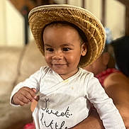 Connor a rejoint le concours — aidez-le/la à gagner de superbes lots ! toddler, child, baby, straw_hat, white_onesie, smiling, portrait, indoor, person, cute, happy, hand, adult_arm, blurred_background, face, infant, clothing, holding, skin, headwear