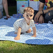 Luca is registered to the contest to win money with this photo: baby, child, toddler, crawling, outdoor, grass, blanket, gift_bags, people, adult, casual_clothing, sunlight, daylight, portrait, cute, summer, family, celebration, happy, event