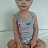Luca is registered to the contest to win money with this photo: toddler, child, sitting, cross_legged, tank_top, gray_clothing, cute, indoor, white_background, barefoot, short_hair, curious_eyes, playful, patterned_clothing, young_child, person, portrait, casual, soft_surface, innocent