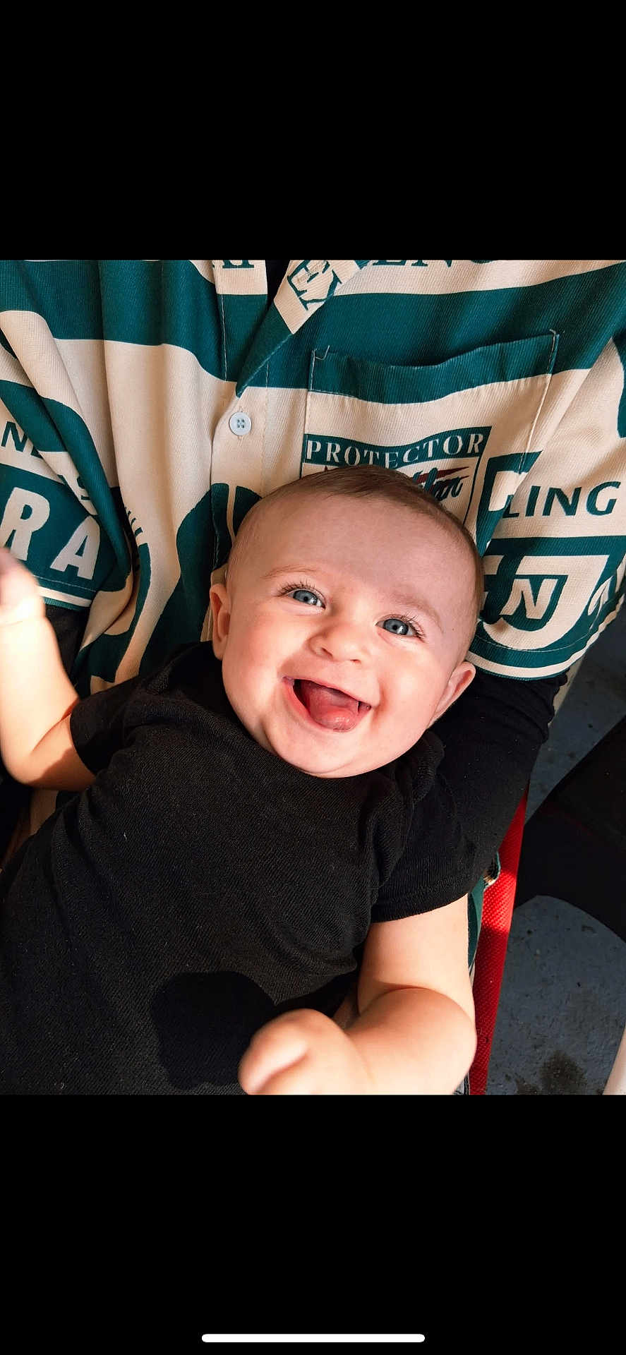Viv joined the competition — help win amazing prizes! baby, child, smiling, happy, face, blue_eyes, black_shirt, person, holding, lap, patterned_clothing, green_color, white_color, indoors, infant, cute, joy, tongue_out, skin, human