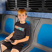 Maxwell joined the competition — help win amazing prizes! child, boy, smiling, seated, public_transport, bus, vehicle_interior, blue_seats, tablet, electronics, black_shirt, shorts, red_hair, portrait, indoors, travel, commuter, ventilation, casual_clothing, happy