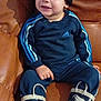 toddler, child, beanie, hat, adidas, tracksuit, rain_boots, owl, blue, leather_couch, indoor, sitting, cute, smiling, casual_clothing, footwear, portrait, young_child, cozy, happy