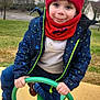 child, boy, winter_clothing, hat, jacket, playground, seesaw, outdoor, smiling, blue_eyes, green_handle, red_scarf, casual_wear, park, trees, grass, houses, play, cold_weather, fun