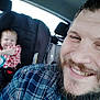 Edward is registered to the contest to win money with this photo: car_interior, child, toddler, car_seat, smiling, man, beard, plaid_shirt, red_shirt, seatbelt, window, headrest, happy, portrait, family, travel, inside_car, casual, daylight, fun
