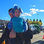 Edward joined the competition — help win amazing prizes! toddler, child, costume, blue, outdoor, sunny, sky, clouds, balloons, parking_lot, adult, person, holding, festival, event, trees, vehicle, black_jacket, cute, playful