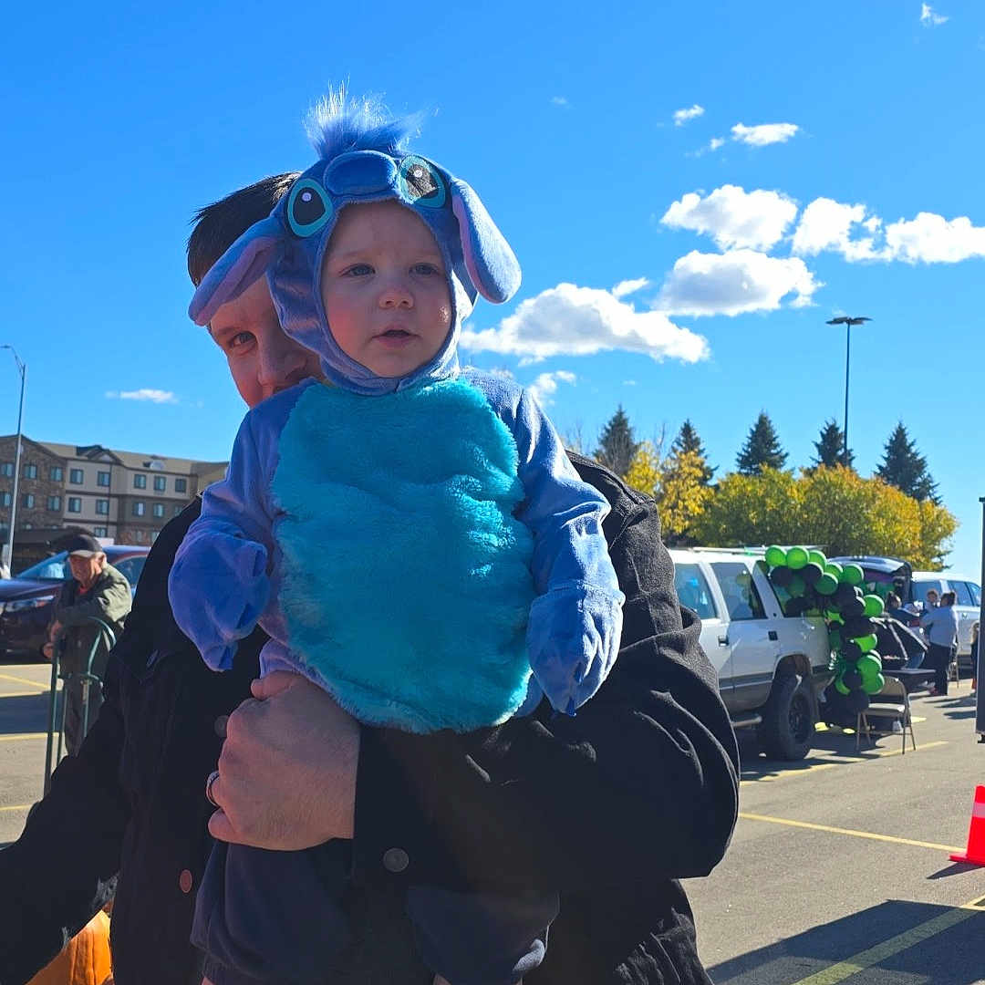 Edward joined the competition — help win amazing prizes! adult, balloons, black_jacket, blue, child, clouds, costume, cute, event, festival, holding, outdoor, parking_lot, person, playful, sky, sunny, toddler, trees, vehicle