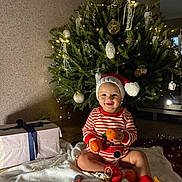 Miron a rejoint le concours — aidez-le/la à gagner de superbes lots ! baby, child, christmas_tree, holiday, festive, santa_hat, tangerines, gift_box, blanket, indoors, decorations, smiling, red_socks, striped_clothing, cozy, lighting, holiday_cheer, cute, celebration, christmas