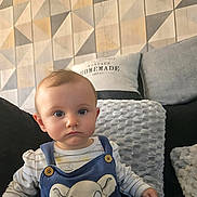 Romy a rejoint le concours — aidez-le/la à gagner de superbes lots ! baby, child, infant, blue_overall, cartoon_lion, couch, cushions, striped_shirt, indoor, portrait, serious_expression, wall_pattern, home, seated, cute, young_child, face, person, comfortable, soft_textures