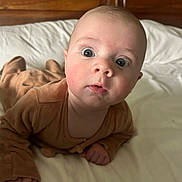 Nino a rejoint le concours — aidez-le/la à gagner de superbes lots ! baby, infant, bed, brown_clothing, wide_eyes, curious, expression, headboard, white_bed_sheet, portrait, indoors, child, cute, young, skin, face, person, hands, lying_down, soft_lighting