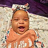 baby, infant, child, smiling, happy, portrait, face, bow, headband, floral_clothing, orange_shirt, hello_shirt, footprints, blanket, floral_blanket, lying_down, indoors, close_up, looking_at_camera, baby_photography