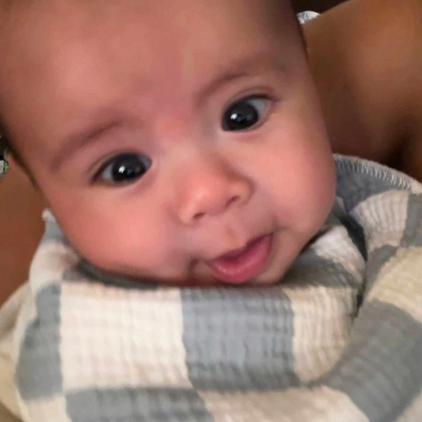 Carlyle Leonardo joined the competition — help win amazing prizes! adult_arm, baby, baby_clothing, blanket, bundled, child, close_up, cream, curious, cute, eyes, face, gray, indoor, infant, photograph, portrait, smile, soft_lighting, swaddled