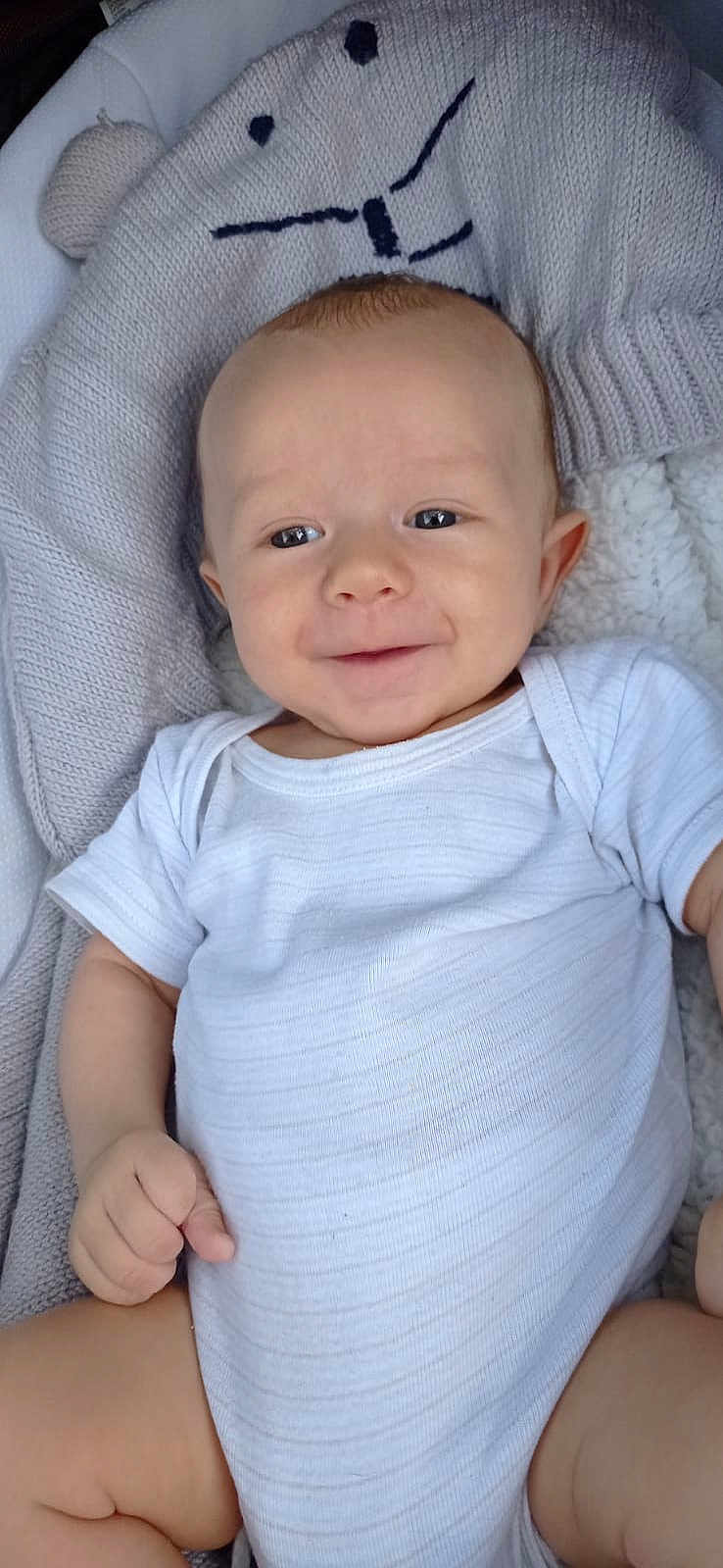 Mayson a rejoint le concours — aidez-le/la à gagner de superbes lots ! baby, infant, smile, white_onesie, knitted_blanket, bear_face_design, cozy, cute, child, lying_down, soft_texture, happy, portrait, skin, young_child, indoor, relaxed, small_hand, baby_clothing, comfort