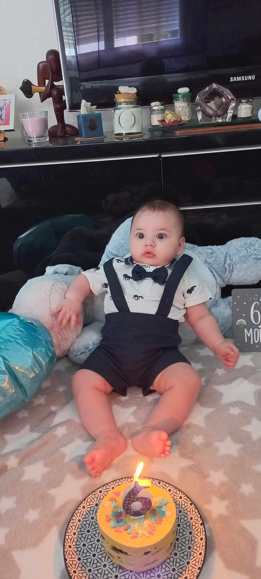 Kamil participe au concours pour gagner de l'argent avec cette photo : baby, infant, birthday_cake, candle, clothing, bow_tie, suspenders, blanket, star_pattern, plush_toy, floor, home_interior, television, decor, plate, celebration, child, sitting, cute, indoor