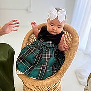 Ellie is registered to the contest to win money with this photo: baby, child, wicker_chair, white_bow, headband, green_dress, plaid, sitting, indoor, hand, adult_hand, floor, minimalist, soft_lighting, woven, cute, portrait, infant, clothing, person