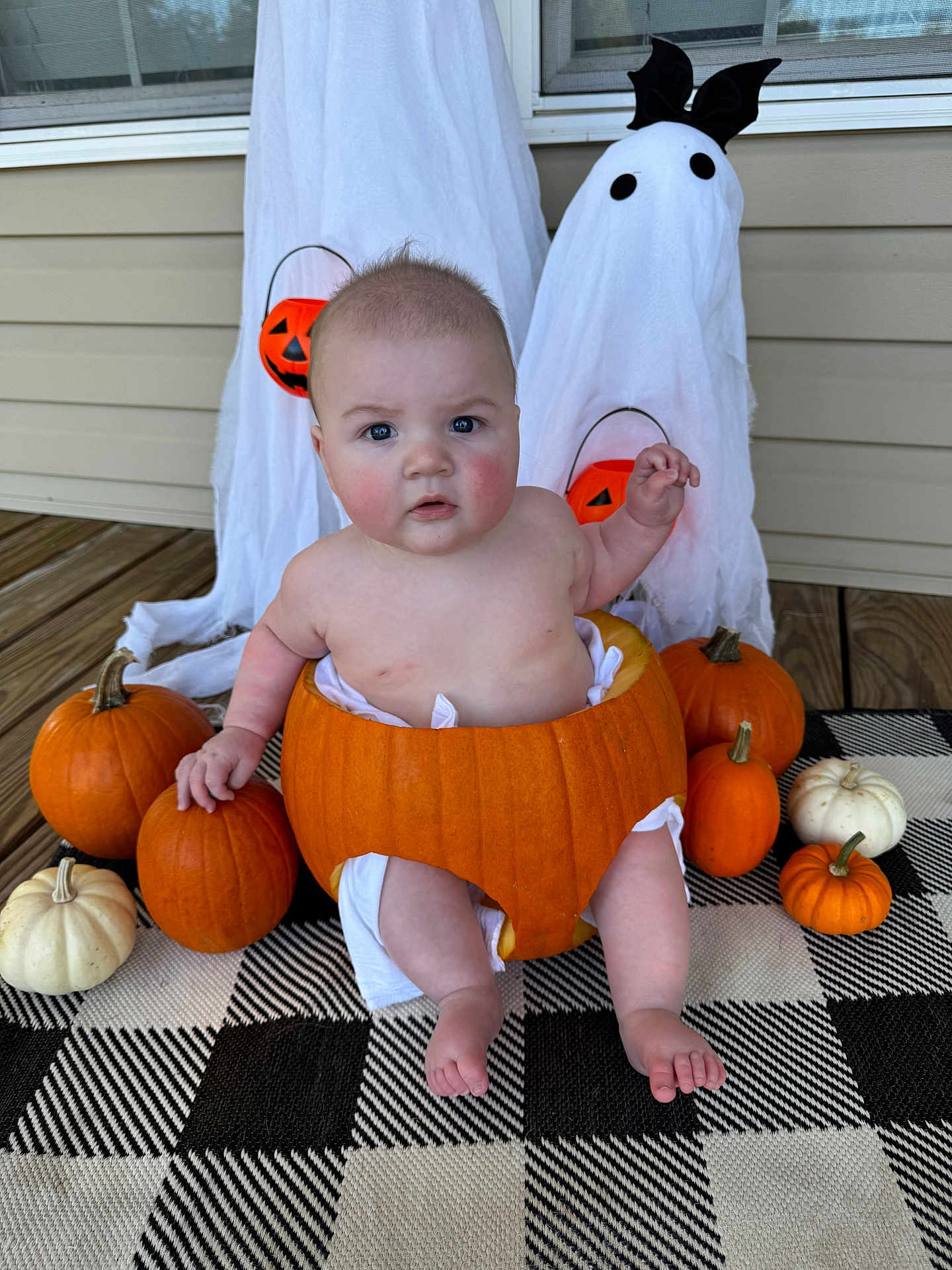 Aaron joined the competition — help win amazing prizes! baby, pumpkin, halloween, ghost_decoration, orange, white, plaid_rug, porch, decorations, child, cute, holiday, seasonal, festive, costume, face, sitting, barefoot, indoor, expression