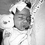 baby, sleeping, pacifier, headband, bow, plush_toy, winnie_the_pooh, blanket, infant, cute, closeup, soft_texture, hand, peaceful, monochrome, portrait, child, indoors, resting, cozy