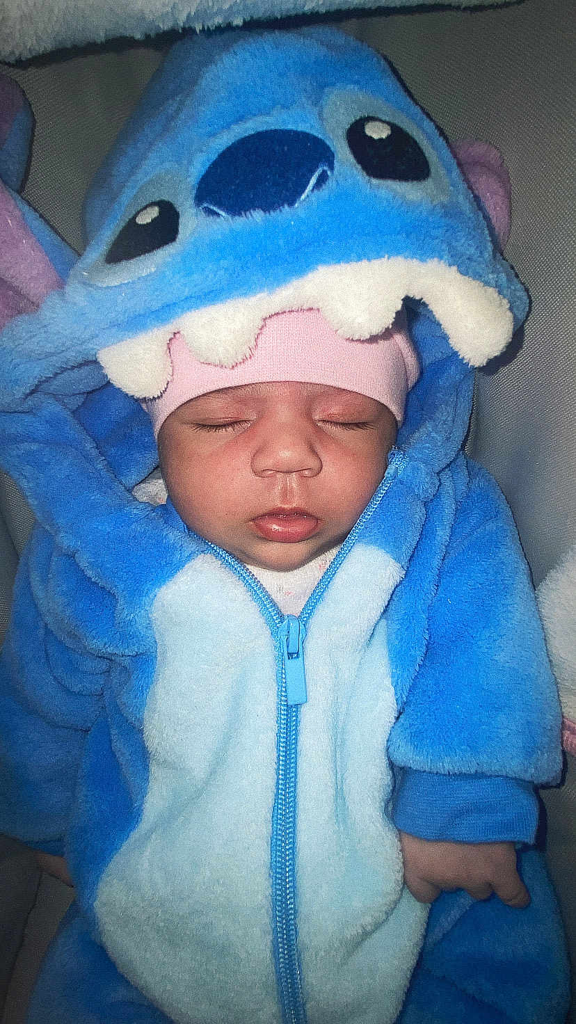 Elyn a rejoint le concours — aidez-le/la à gagner de superbes lots ! baby, sleeping, blue_onesie, hood, child, cute, infant, soft, warm, cozy, pink_hat, closeup, face, hands, zipper, plush, adorable, costume, indoor, resting