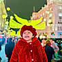 child, toddler, red_coat, hat, smiling, outdoor, night, holiday_lights, city_street, people, crowd, festive, winter_clothing, happy, portrait, urban, celebration, bright_lights, warm_clothing, festival