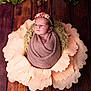 newborn, baby, flower_petals, headband, wrapped, blanket, wooden_floor, greenery, garland, soft_lighting, portrait, cute, infant, decorative, indoors, peaceful, wrapped_baby, pink, brown, flower