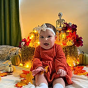 Mariposa is registered to the contest to win money with this photo: baby, child, infant, smiling, portrait, sitting, indoors, halloween, autumn, pumpkins, skeleton, flowers, leaves, festive, costume, headband, dress, socks, bed, string_lights