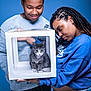 affection, blue_background, cat, cat_paws, curious_expression, denim, dreadlocks, earrings, holding, indoor, kitten, necklace, pet_owner, portrait, smile, studio, sweatshirt, two_people, white_box, young_adults