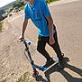 boy, child, scooter, blue_shirt, black_pants, outdoor, road, shadow, sunny, fence, grass, car, rural, sidewalk, sport_shirt, casual_clothing, person, daylight, vehicle, transportation