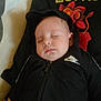 baby, sleeping, hoodie, black_clothing, nike_logo, infant, pillow, resting, peaceful, indoor, child, young_child, face, person, cute, calm, comfort, soft, portrait, closeup