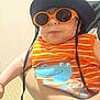 baby, child, orange_sunglasses, hat, striped_clothing, cartoon_print, person, arm, indoor, holding, cute, smiling, fashion, accessory, infant, portrait, playful, funny, bright_colors, casual