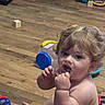 baby, bare_chested, blocks, blond_hair, child, colorful_objects, curious, curly_hair, face, fingers, hand, indoors, open_mouth, plastic_toy, playroom, portrait, sitting, toddler, toy, wooden_floor