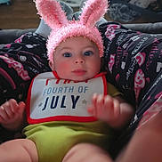 Emmett joined the competition — help win amazing prizes! baby, bunny_ears, headband, bib, green_clothing, person, indoor, lap, pants, patterned_clothing, face, child, cute, blue_eyes, pink, soft_texture, furniture, home, floor, legs