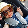Inaya participe au concours pour gagner de l'argent avec cette photo : baby, baby_toy, blue_clothing, car_seat, child, cute, hand, happy, hat, headwear, infant, outdoor, person, playful, seat, seatbelt, smile, sunglasses, sunlight, tongue_out
