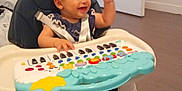 Inaya a rejoint le concours — aidez-le/la à gagner de superbes lots ! baby, child, clothing, door, face, feet, floor, furniture, hand, happy, head, high_chair, indoor, music_toy, person, playing, room, seat_belt, smiling, toy_keyboard