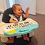 baby, child, clothing, door, face, feet, floor, furniture, hand, happy, head, high_chair, indoor, music_toy, person, playing, room, seat_belt, smiling, toy_keyboard