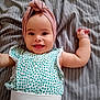 arms_up, baby, child, cute, face, happy, head_wrap, headwear, indoor, infant, lying_down, patterned_clothing, person, portrait, skin, smiling, soft, striped_blanket, textile, young_child