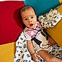 Inaya a rejoint le concours — aidez-le/la à gagner de superbes lots ! baby, blanket, blue, child, colorful_chair, cute, expression, furniture, indoor, infant, onesie, patterned_blanket, person, portrait, red, sitting, surprised_expression, white, yellow, young_child