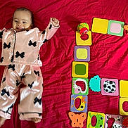 Inaya participe au concours pour gagner de l'argent avec cette photo : baby, black_bows, bright_colors, child, colorful_toys, cute, happy, indoor, infant, lying_down, pajamas, pattern, pink_clothing, playtime, raised_arms, red_blanket, small_feet, smiling, soft_fabric, toy_blocks