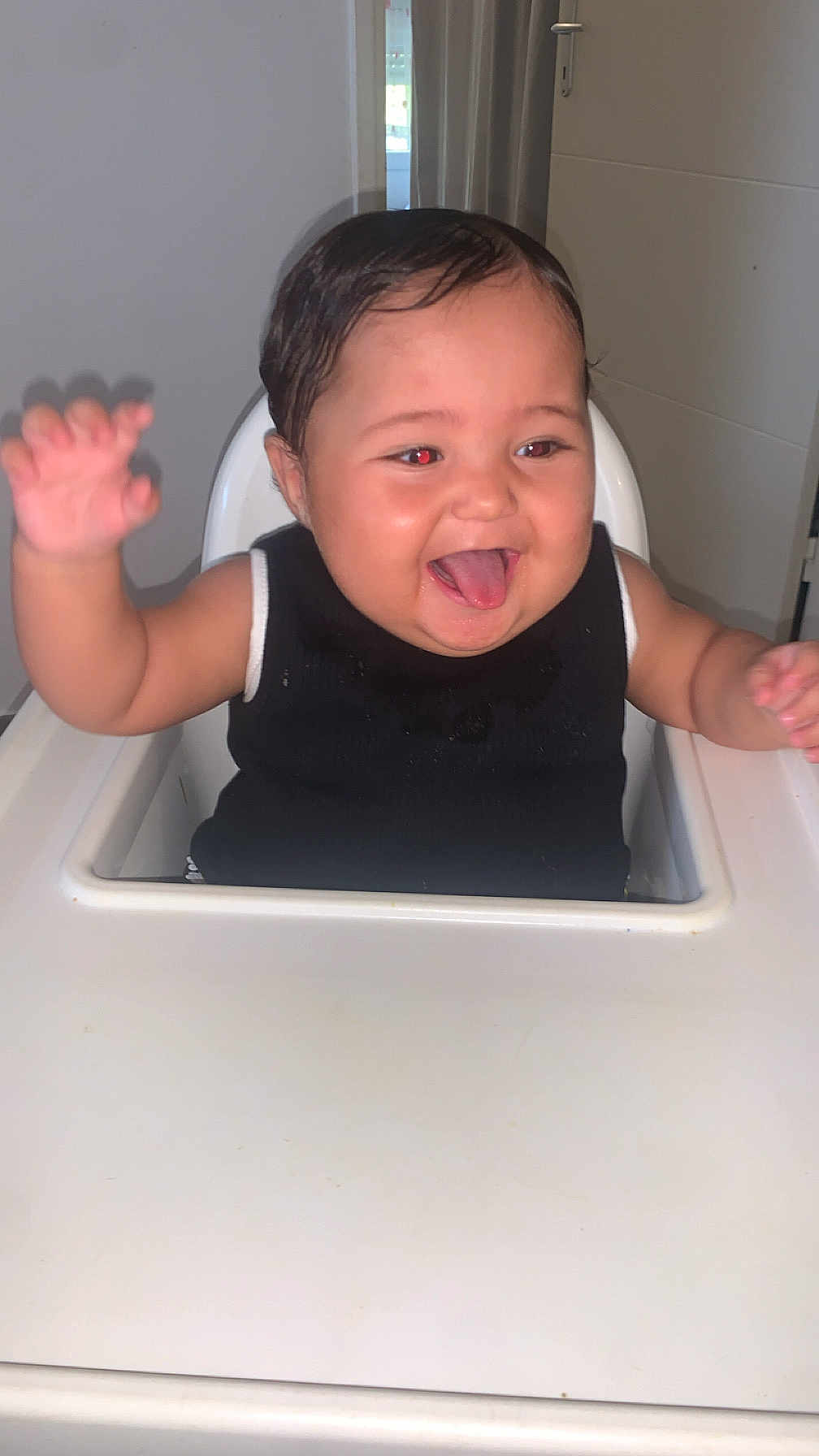Djenna participe au concours pour gagner de l'argent avec cette photo : baby, high_chair, indoor, smiling, tongue_out, arm_raised, black_clothing, face, child, person, happy, cute, furniture, infant, short_hair, skin, tongue, red_eye, waving, playful