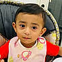 Krish is registered to the contest to win money with this photo: baby, bib, child, clothing, curious, cute, earrings, expression, face, feeding, high_chair, home, indoor, looking_at_camera, person, portrait, red_shirt, seated, toddler, young_child
