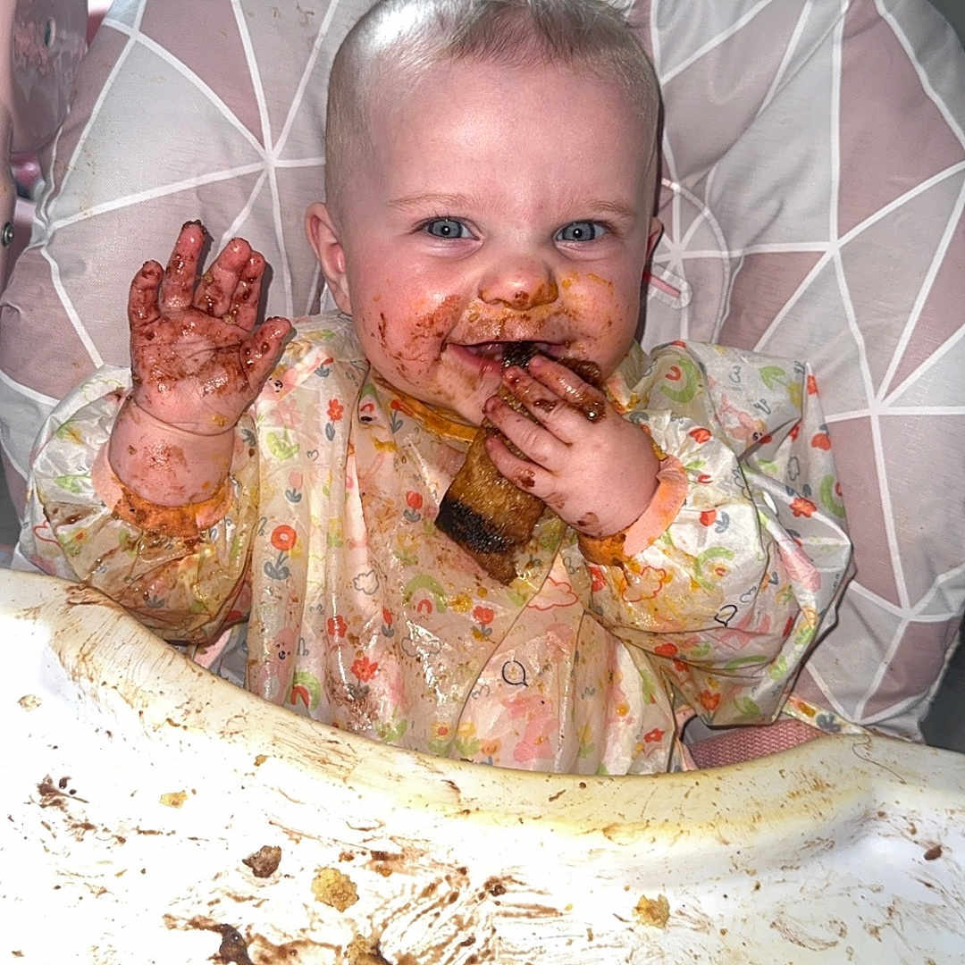 Maddison joined the competition — help win amazing prizes! baby, bib, child, clothing, cute, eating, face, food, fun, hands, happy, high_chair, indoor, kitchen, messy, person, plate, playful, smiling, table