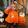 child, toddler, baby, smiling, waving, halloween, pumpkin, jack_o_lantern, skeleton, costume, orange_clothing, headband, fireplace, stone, indoor, sitting, portrait, happy, seasonal_decor, family_photo