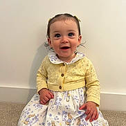 Ayla joined the competition — help win amazing prizes! baby, child, girl, smiling, yellow_cardigan, floral_dress, bunny_prints, hair_bows, carpet, indoor, cute, happy, portrait, sitting, long_sleeves, wall, clothing, person, infant, toddler