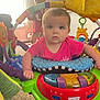 Leanna is registered to the contest to win money with this photo: baby, child, indoor, activity_jumper, colorful_toys, carpet, window, curtain, red_shirt, play, infant, person, toy, bright_colors, face, expression, young_child, background, hand, furniture