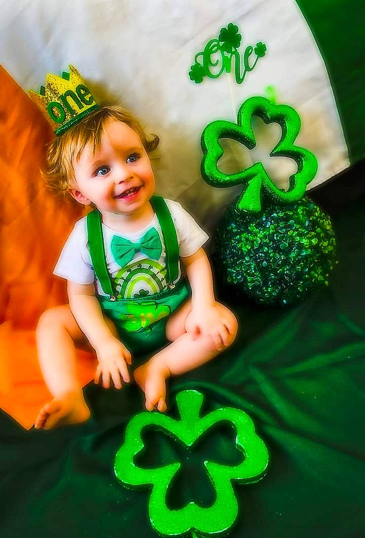 Royal is registered to the contest to win money with this photo: baby, baby_toddler_clothing, child, circle, clover, event, font, grass, green, happy, holiday, joy, pattern, people_in_nature, person, play, shamrock, sitting, smile, symbol